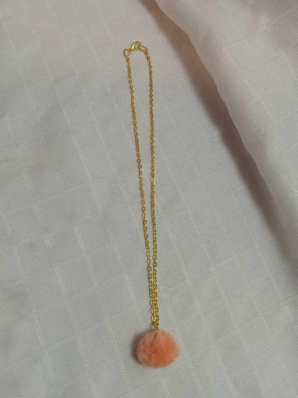 Handmade necklace with a small pom-pom and gold-colored accent hooks and chains